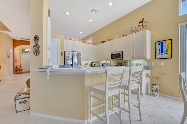 kitchen with a kitchen breakfast bar, white cabinetry, light tile patterned flooring, kitchen peninsula, and stainless steel appliances