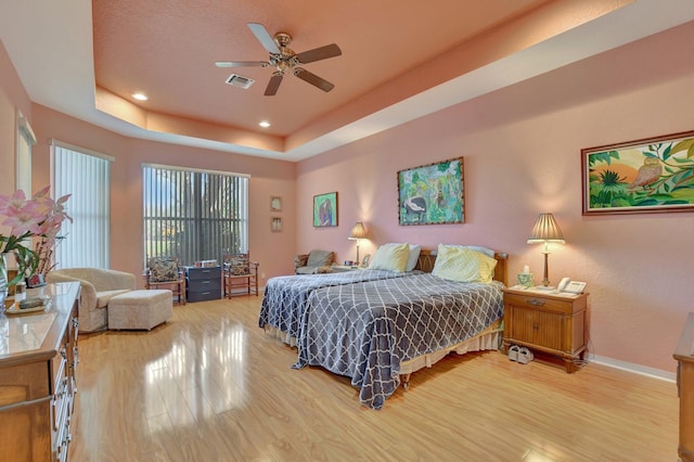 bedroom with ceiling fan, light hardwood / wood-style floors, and a tray ceiling