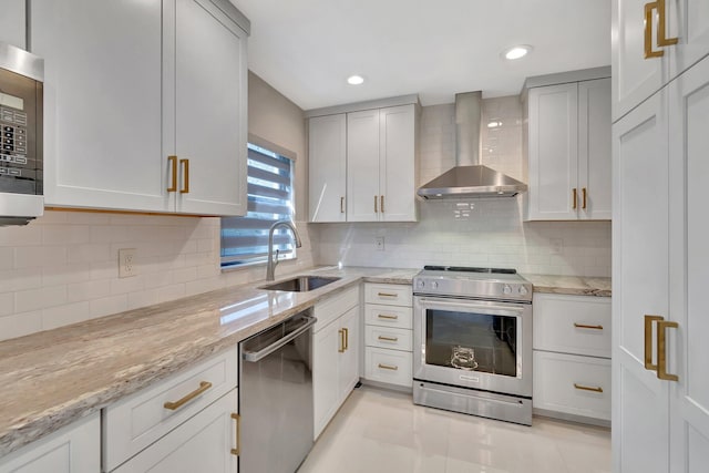 kitchen with light stone countertops, sink, wall chimney exhaust hood, light tile patterned flooring, and appliances with stainless steel finishes