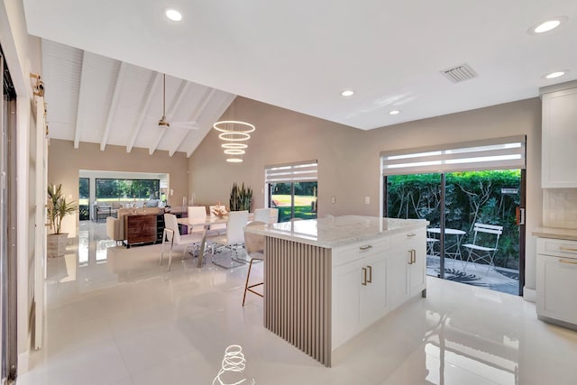 kitchen featuring decorative light fixtures, white cabinetry, vaulted ceiling with beams, a kitchen island, and light tile patterned flooring