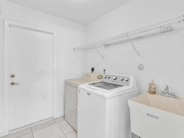 clothes washing area with light tile patterned floors, sink, and washing machine and clothes dryer