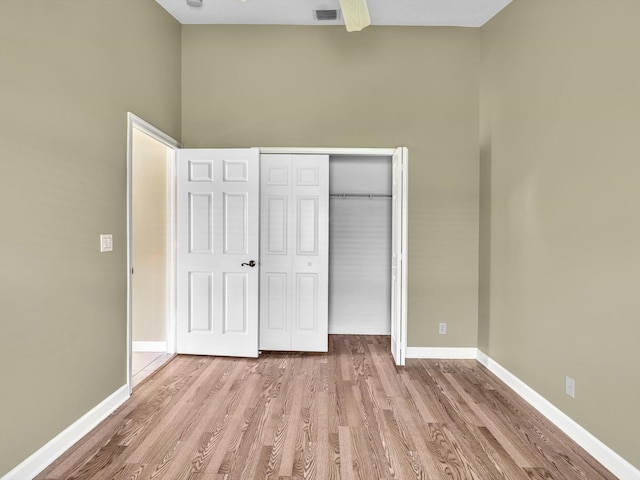 unfurnished bedroom featuring a closet, a towering ceiling, and light hardwood / wood-style flooring