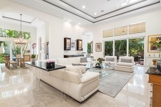 living room featuring a raised ceiling, ornamental molding, a high ceiling, and an inviting chandelier