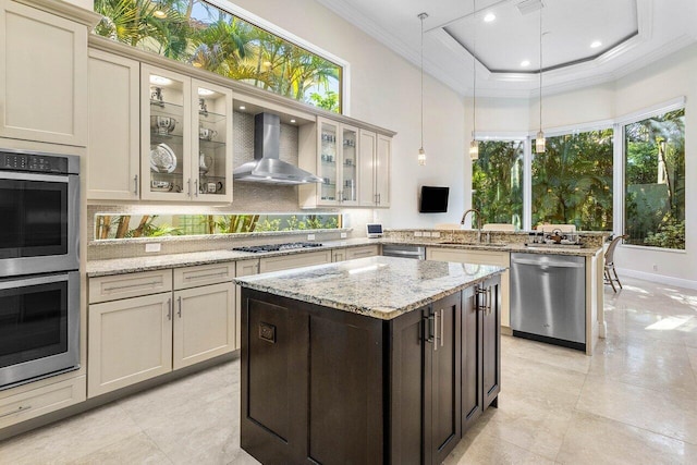 kitchen with appliances with stainless steel finishes, sink, wall chimney range hood, decorative light fixtures, and cream cabinetry