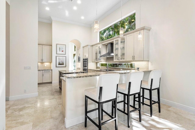 kitchen with kitchen peninsula, a breakfast bar, a high ceiling, and wall chimney range hood