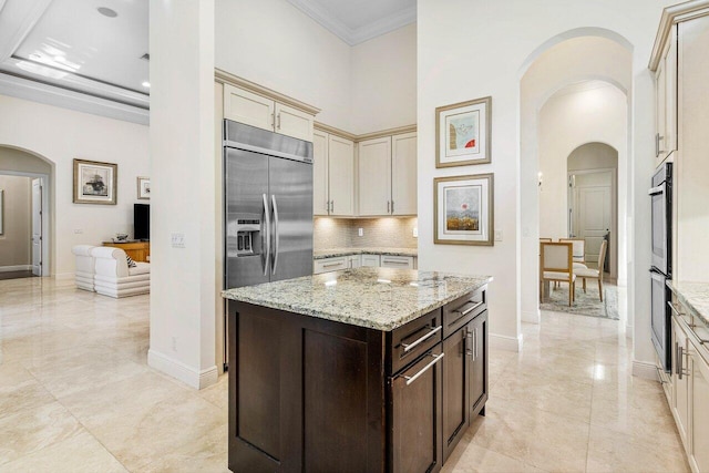 kitchen with dark brown cabinetry, light stone countertops, cream cabinetry, a kitchen island, and appliances with stainless steel finishes