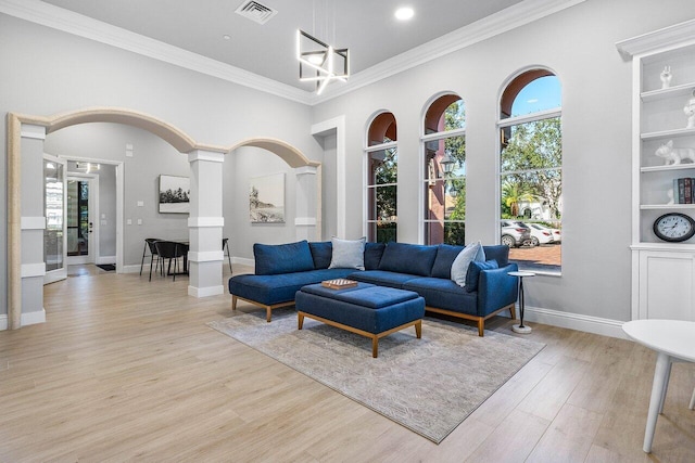 living room with ornate columns, built in shelves, an inviting chandelier, light wood-type flooring, and ornamental molding