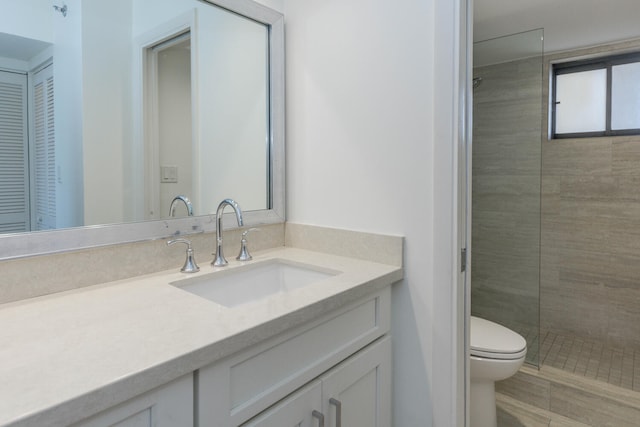 bathroom featuring a tile shower, vanity, and toilet