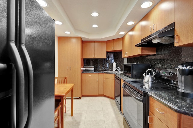 kitchen featuring sink, dark stone counters, a tray ceiling, light tile patterned floors, and black appliances