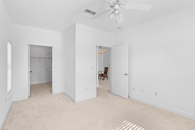 unfurnished bedroom featuring a walk in closet, ceiling fan, a closet, and light carpet