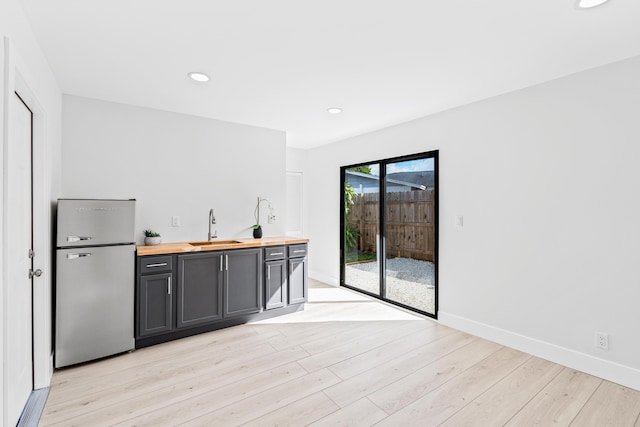 bar with butcher block countertops, stainless steel refrigerator, light hardwood / wood-style floors, and sink