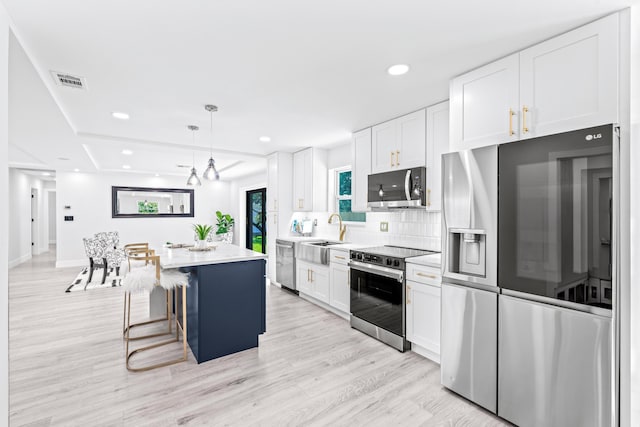 kitchen with stainless steel appliances, decorative light fixtures, white cabinets, light hardwood / wood-style floors, and a kitchen island