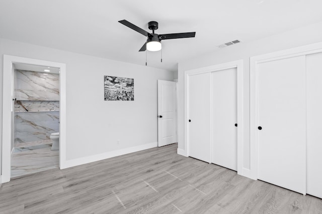 unfurnished bedroom featuring ceiling fan, light hardwood / wood-style floors, connected bathroom, and two closets