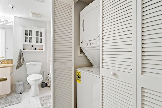 clothes washing area featuring stacked washer / dryer, light tile patterned flooring, and a textured ceiling