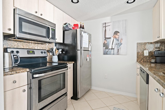 kitchen featuring white cabinets, dark stone counters, a textured ceiling, light tile patterned floors, and appliances with stainless steel finishes