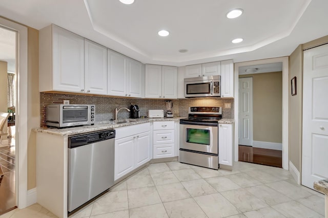 kitchen featuring a raised ceiling, backsplash, stainless steel appliances, and white cabinetry