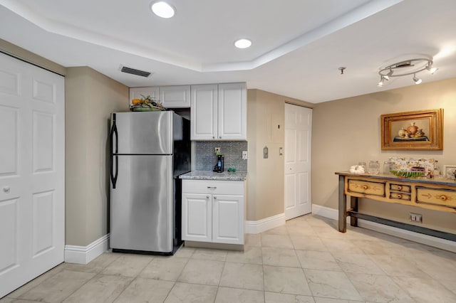 kitchen featuring white cabinetry, light stone countertops, a raised ceiling, backsplash, and stainless steel fridge