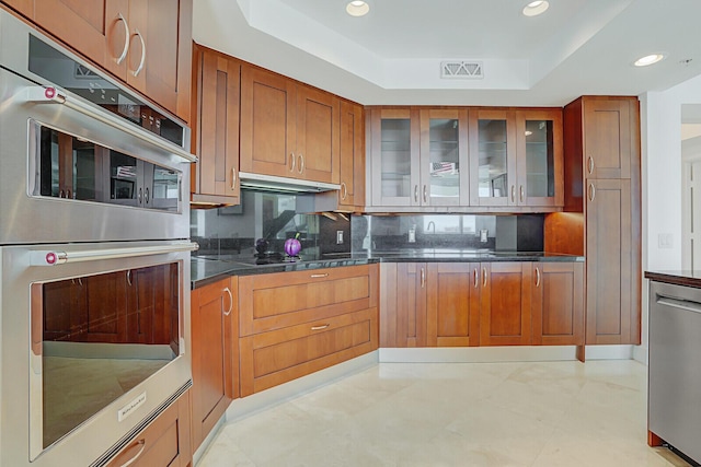 kitchen with appliances with stainless steel finishes, backsplash, dark stone counters, and a tray ceiling