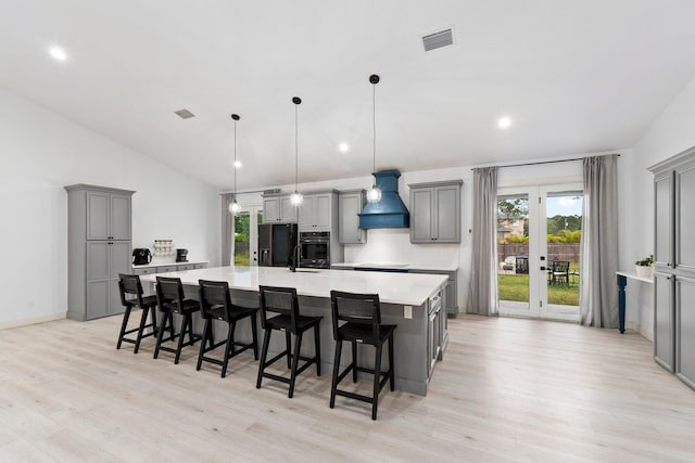 kitchen with gray cabinetry, a large island, stainless steel oven, pendant lighting, and custom range hood