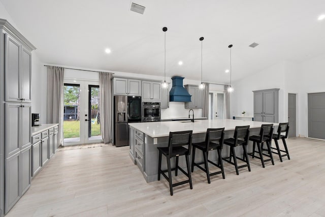 kitchen featuring appliances with stainless steel finishes, a kitchen breakfast bar, gray cabinetry, pendant lighting, and a large island with sink