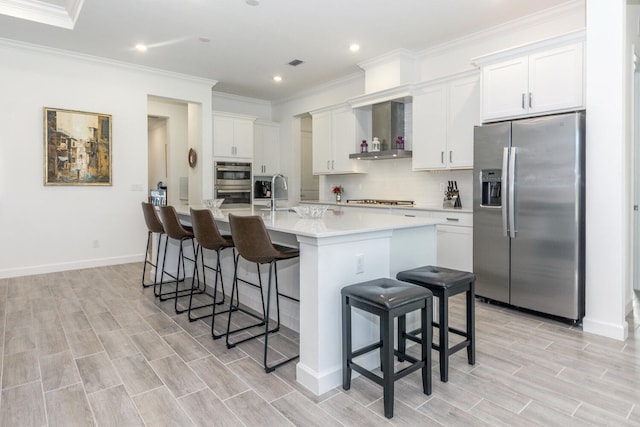 kitchen with a kitchen island with sink, white cabinets, wall chimney range hood, and appliances with stainless steel finishes