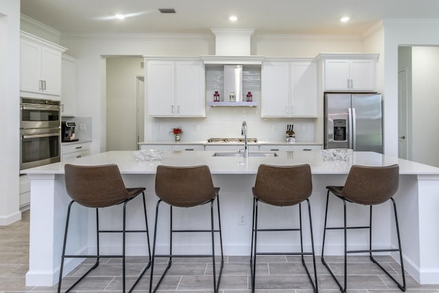 kitchen with a breakfast bar area, white cabinets, an island with sink, and appliances with stainless steel finishes