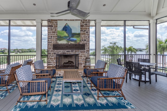 sunroom with a water view, a stone fireplace, and ceiling fan