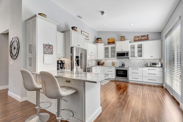 kitchen featuring a healthy amount of sunlight, lofted ceiling, stainless steel appliances, and white cabinetry