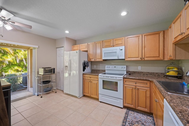 kitchen with dark countertops, light tile patterned floors, white appliances, a ceiling fan, and a sink