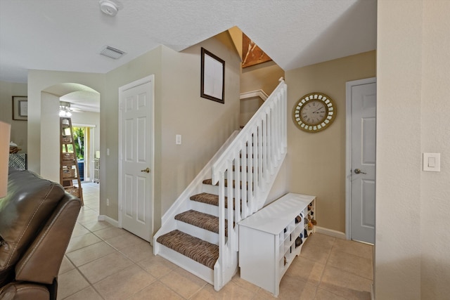 staircase featuring tile patterned flooring, visible vents, baseboards, and ceiling fan