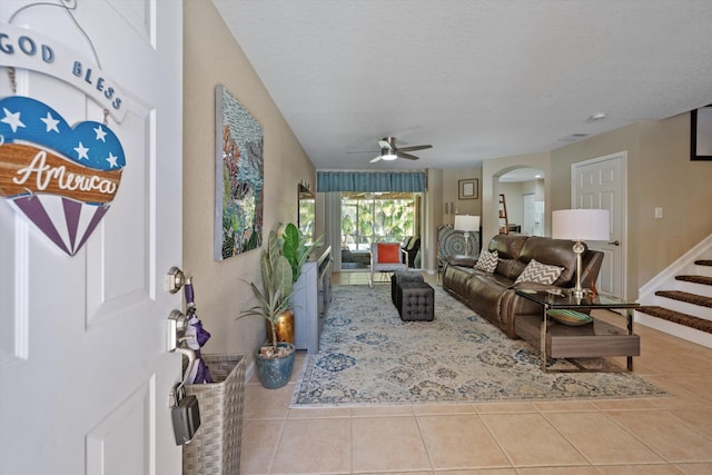 living area featuring stairway, arched walkways, tile patterned floors, a textured ceiling, and a ceiling fan