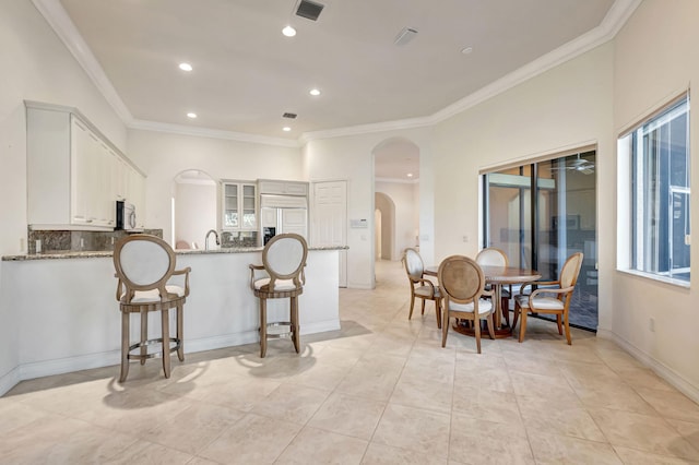 kitchen with white cabinetry, kitchen peninsula, light stone counters, and ornamental molding