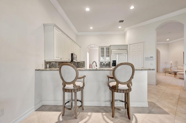 kitchen featuring kitchen peninsula, backsplash, light stone counters, paneled fridge, and white cabinetry