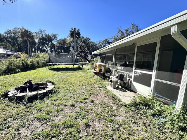 view of yard with a sunroom, a trampoline, and an outdoor fire pit