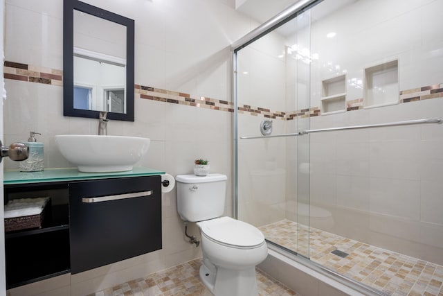 bathroom featuring a shower with door, vanity, tile walls, and toilet