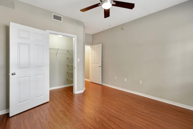 unfurnished bedroom featuring a spacious closet, ceiling fan, wood-type flooring, and a closet