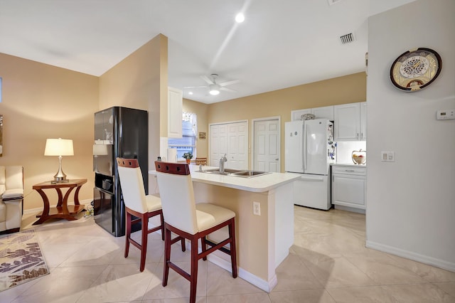 kitchen with white cabinetry, sink, ceiling fan, white refrigerator, and a breakfast bar area