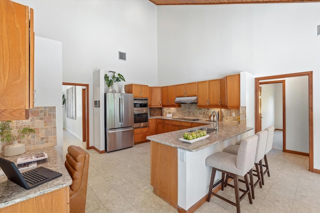 kitchen featuring kitchen peninsula, a kitchen breakfast bar, tasteful backsplash, stainless steel appliances, and high vaulted ceiling