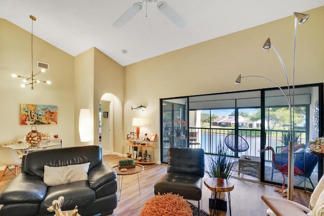 living room with ceiling fan with notable chandelier, light hardwood / wood-style floors, and high vaulted ceiling