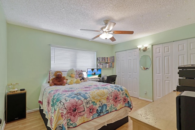 bedroom with a textured ceiling, ceiling fan, two closets, and light wood-type flooring