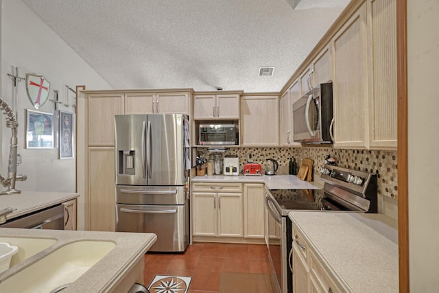 kitchen with sink, stainless steel appliances, a textured ceiling, light brown cabinetry, and dark tile patterned flooring