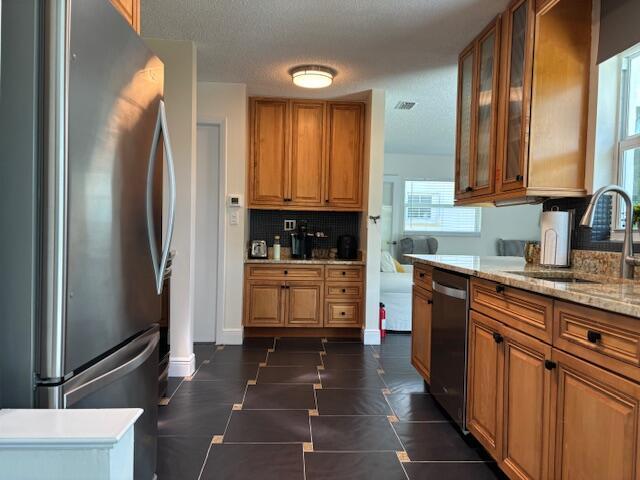 kitchen with sink, a textured ceiling, appliances with stainless steel finishes, light stone countertops, and backsplash