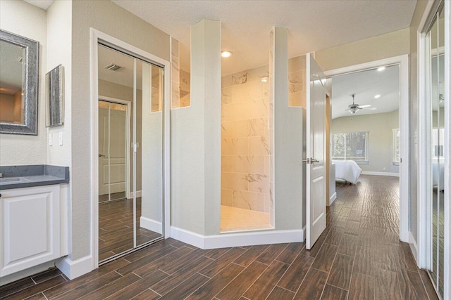 bathroom with ceiling fan, hardwood / wood-style floors, a textured ceiling, tiled shower, and vanity