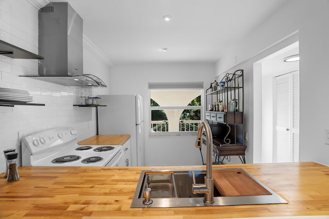 kitchen featuring white appliances, butcher block counters, wall chimney range hood, ornamental molding, and sink