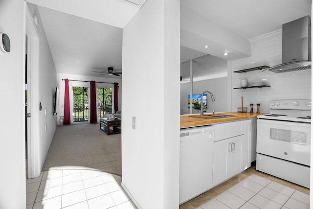 kitchen featuring white appliances, light carpet, white cabinets, wall chimney range hood, and sink