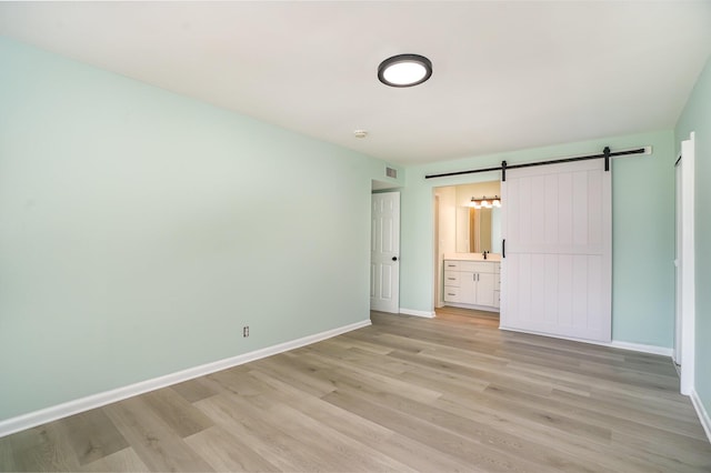 unfurnished bedroom featuring a barn door, ensuite bathroom, and light hardwood / wood-style flooring