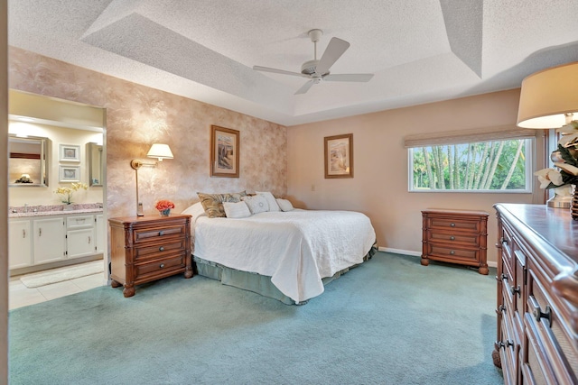 bedroom with ensuite bath, light colored carpet, a raised ceiling, and ceiling fan