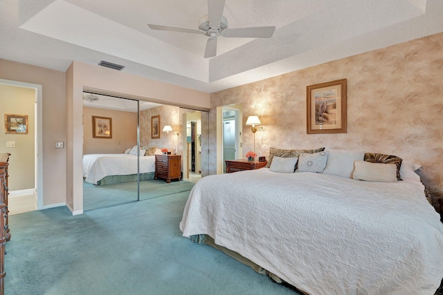 carpeted bedroom featuring ceiling fan, a raised ceiling, and a closet