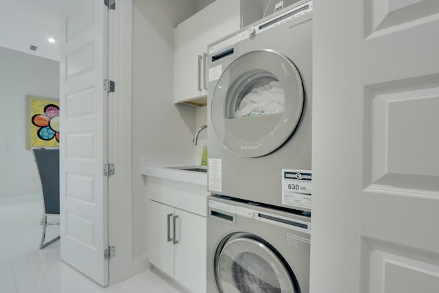 laundry area featuring cabinets, stacked washing maching and dryer, sink, and light tile patterned floors