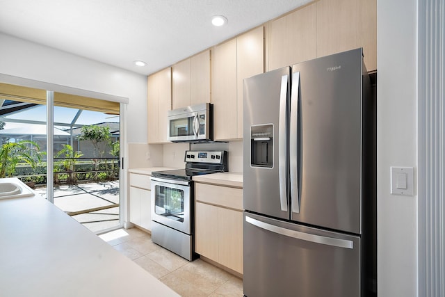 kitchen with light tile patterned flooring, sink, stainless steel appliances, and light brown cabinets